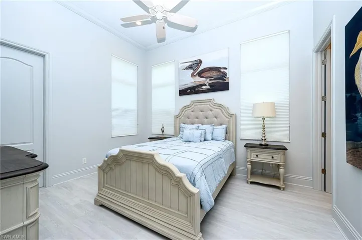 Bedroom with ceiling fan, ornamental molding, and light wood-type flooring