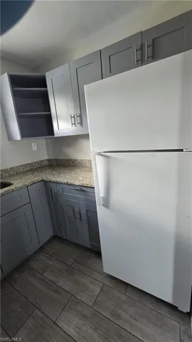 Kitchen featuring gray cabinets, freestanding refrigerator, light stone countertops, open shelves, and wood tiled floors