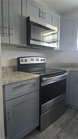 Kitchen with stainless steel appliances, gray cabinets, light stone countertops, and light wood finished floors