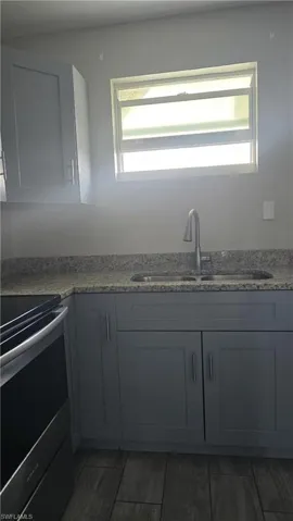 Kitchen with stainless steel range with electric cooktop, light stone countertops, gray cabinets, and dark wood finished floors