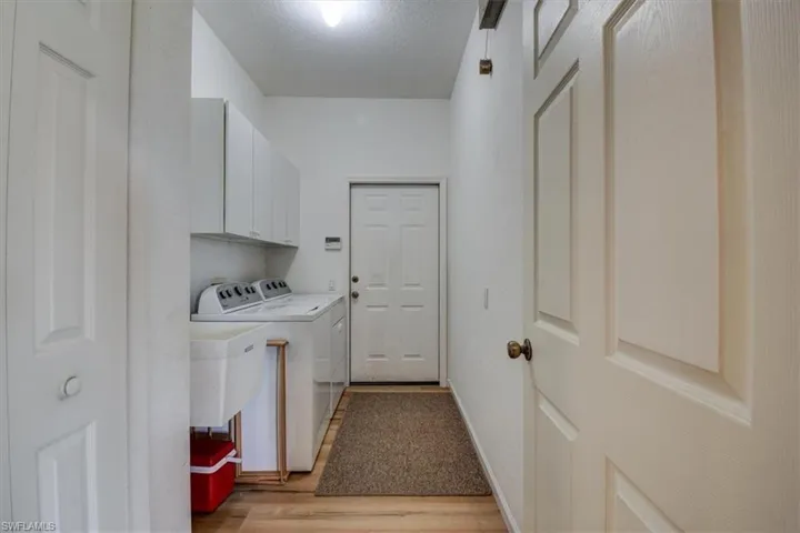 Washroom featuring washer and dryer, light wood finished floors, cabinet space, and a textured ceiling