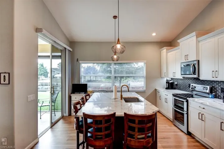 Kitchen with appliances with stainless steel finishes, white cabinetry, decorative light fixtures, a breakfast bar area, and light stone countertops