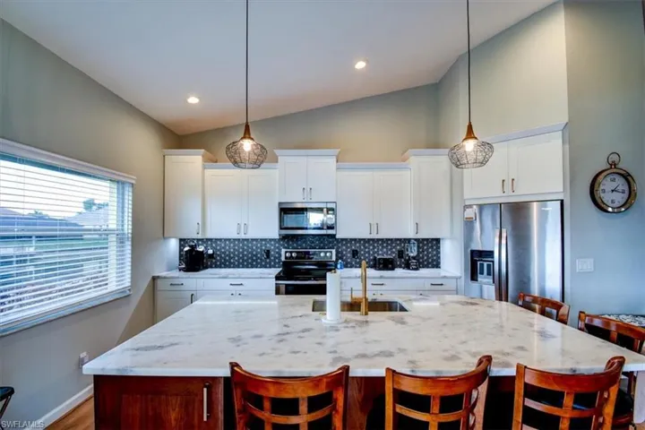 Kitchen with a breakfast bar area, a kitchen island with sink, stainless steel appliances, white cabinets, and recessed lighting