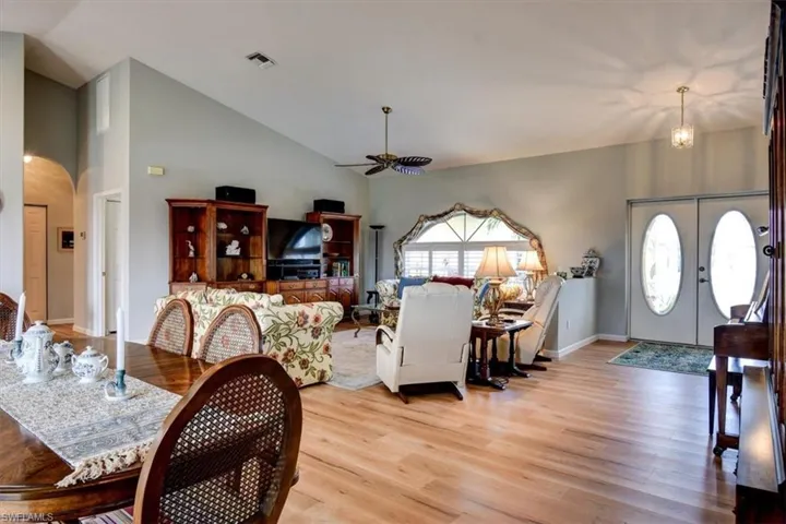 Living area featuring light wood finished floors, high vaulted ceiling, arched walkways, a ceiling fan, and french doors