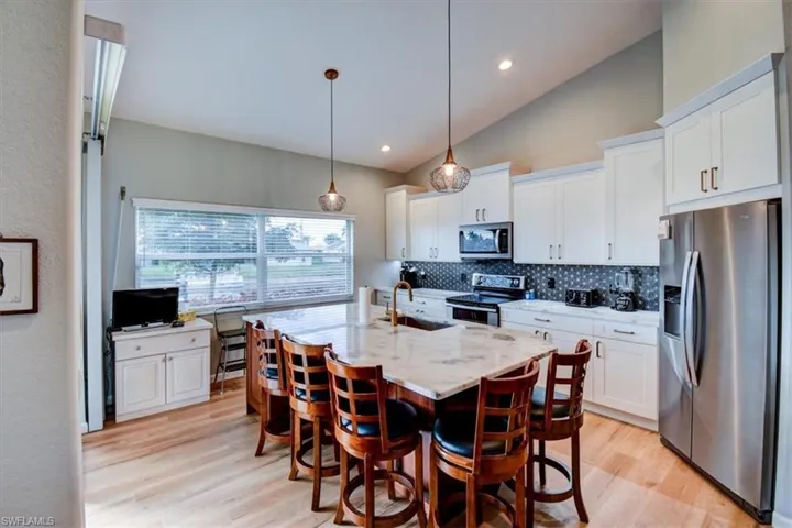 Kitchen featuring appliances with stainless steel finishes, a breakfast bar area, hanging light fixtures, light wood-type flooring, and vaulted ceiling