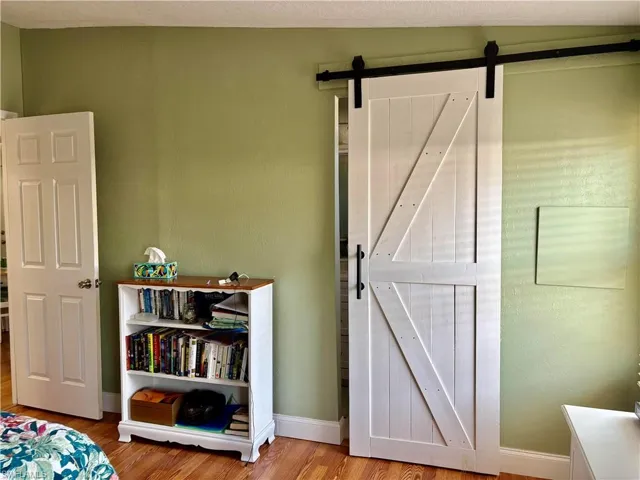 Bedroom with a barn door, wood finished floors, and baseboards