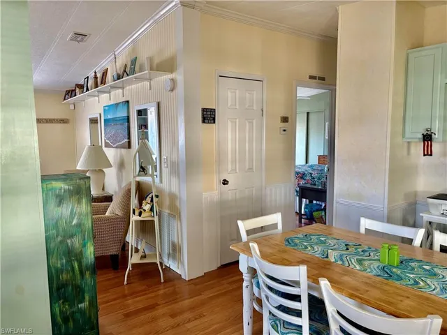 Dining space with wood finished floors, visible vents, ornamental molding, and wainscoting