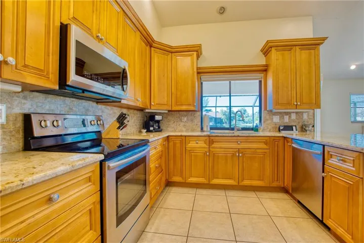 Kitchen featuring appliances with stainless steel finishes, light stone countertops, light tile patterned flooring, decorative backsplash, and brown cabinets