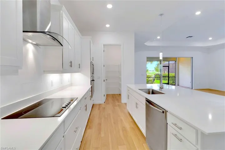 Kitchen featuring white cabinetry, light wood-style flooring, wall chimney exhaust hood, a large island, and recessed lighting