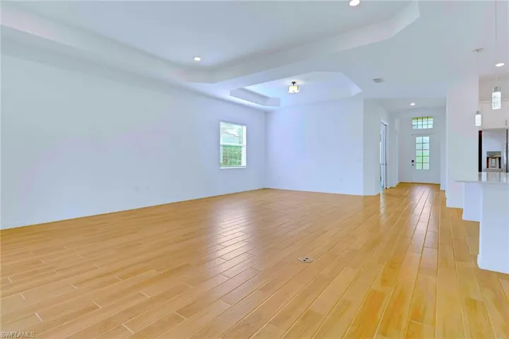 Unfurnished living room with a tray ceiling, plenty of natural light, light wood-style flooring, arched walkways, and recessed lighting