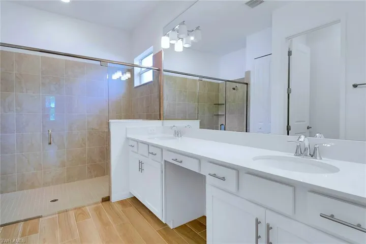 Bathroom featuring double vanity, a shower stall, and wood finish floors