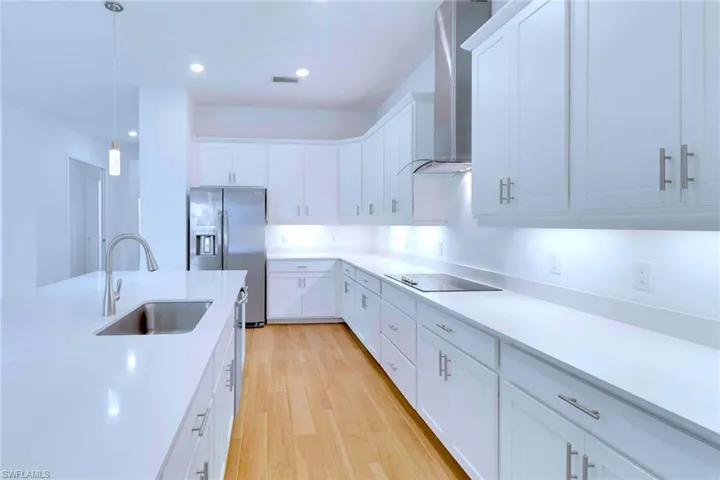 Kitchen featuring white cabinetry, wall chimney range hood, hanging light fixtures, stainless steel fridge, and light wood-style flooring