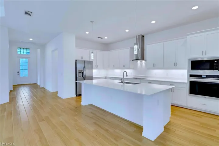 Kitchen featuring stainless steel appliances, white cabinets, recessed lighting, wall chimney range hood, and light wood-style floors