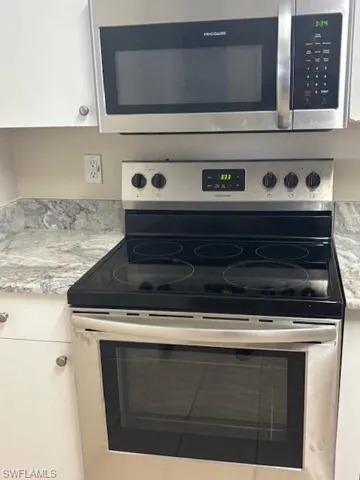 Kitchen view of electric range, light countertops, and white cabinetry