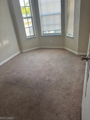 Unfurnished room featuring carpet, baseboards, plenty of natural light, and a textured wall