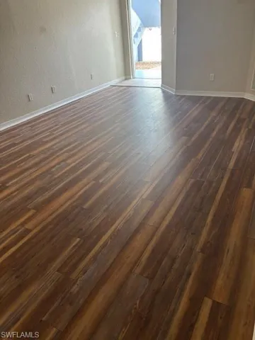 Spare room featuring baseboards, dark wood-style flooring, and a textured wall