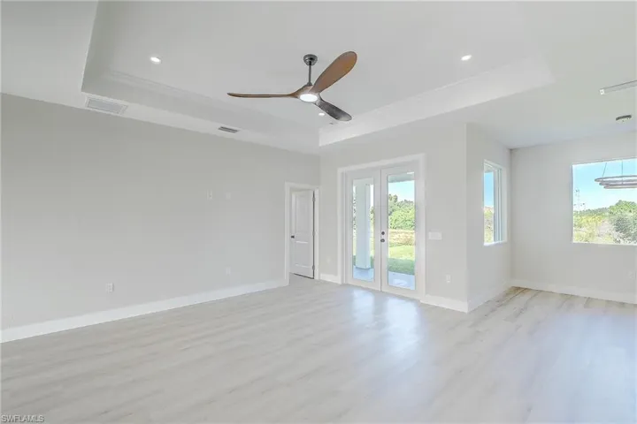 Empty room with a tray ceiling, french doors, light wood-type flooring, a ceiling fan, and recessed lighting