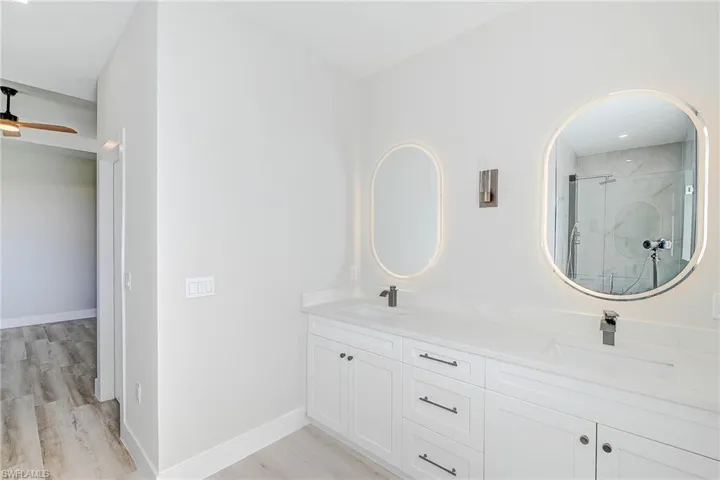 Primary Bathroom featuring a marble finish shower, double vanity, light wood-type flooring, and a ceiling fan