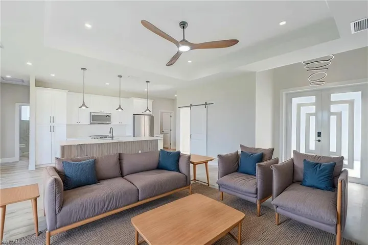 Living room featuring a barn door, a raised ceiling, a ceiling fan, and recessed lighting. Virtual Staged