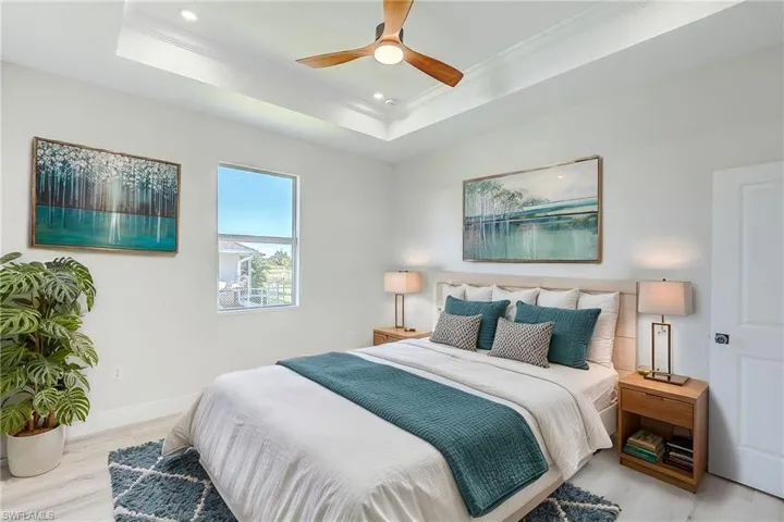 Bedroom featuring wood finished floors, a raised ceiling, ornamental molding, ceiling fan, and recessed lighting. Virtual Staged
