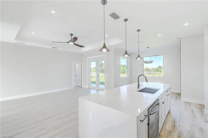 Kitchen featuring a raised ceiling, decorative light fixtures, light wood-style flooring, a center island with sink, and light stone countertops