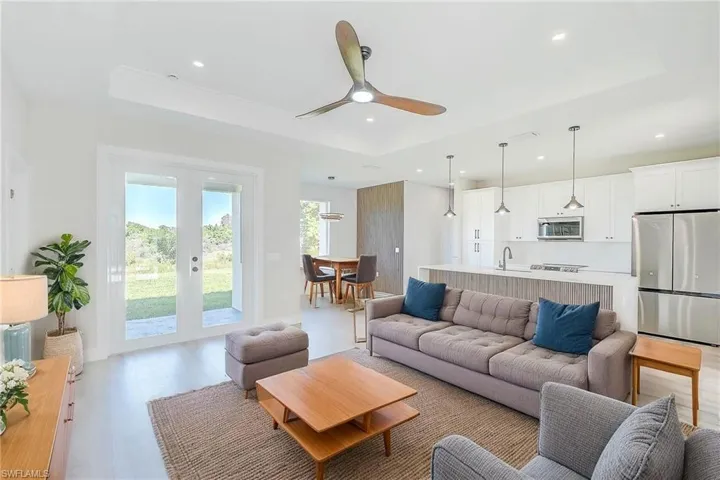 Living area with a tray ceiling, a ceiling fan, french doors, recessed lighting, and light wood finished floors. Virtual Staged