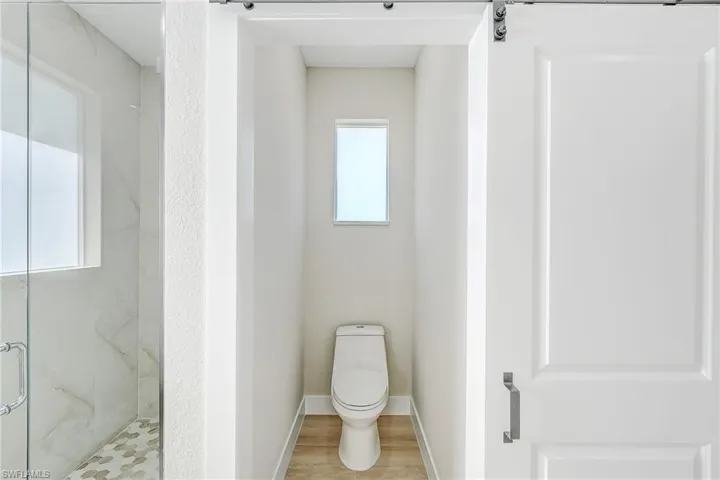 Primary bathroom featuring healthy amount of natural light, a marble finish shower, and wood finished floors