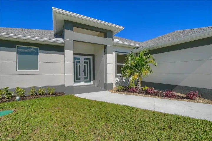 Doorway to property with a lawn, stucco siding, and a shingled roof