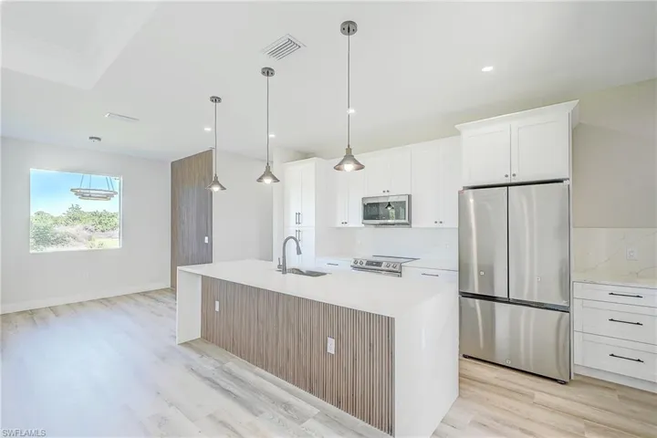 Kitchen featuring appliances with stainless steel finishes, a center island with sink, light stone countertops, white cabinets, and pendant lighting