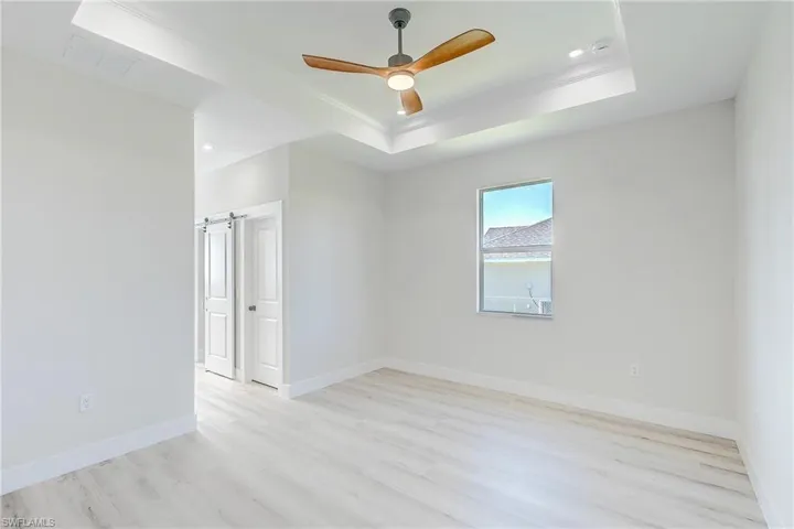 Empty room featuring a tray ceiling, light wood finished floors, a ceiling fan, crown molding, and recessed lighting