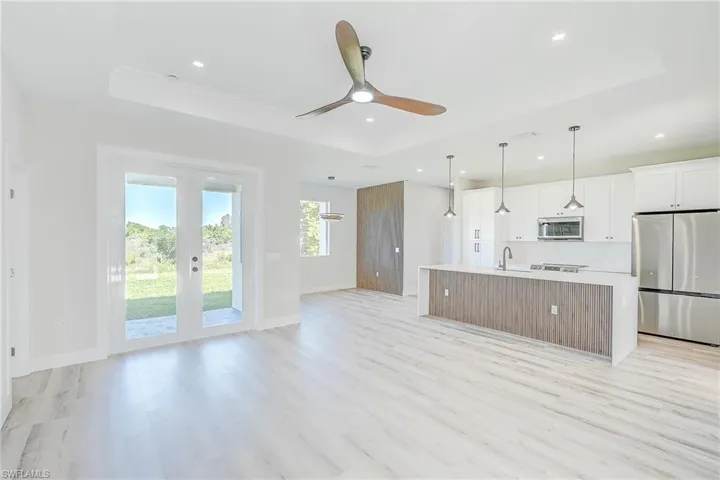 LVR - Kitchen view with a raised ceiling, appliances with stainless steel finishes, an open floor plan, white cabinetry, and a center island with sink
