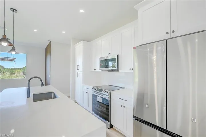 Kitchen featuring stainless steel appliances, hanging light fixtures, white cabinets, recessed lighting, and light stone counters