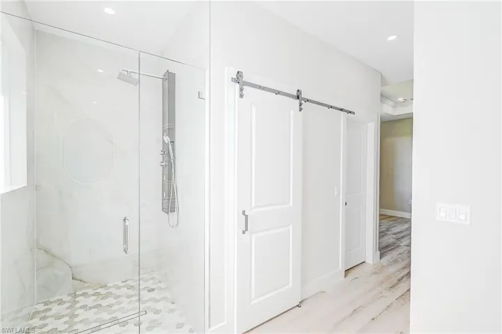 Primary bathroom with a marble finish shower, light wood-style flooring, and recessed lighting