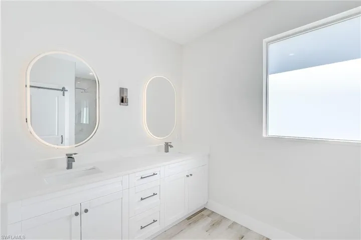 Primary bathroom featuring a shower stall, double vanity, and light wood finished floors