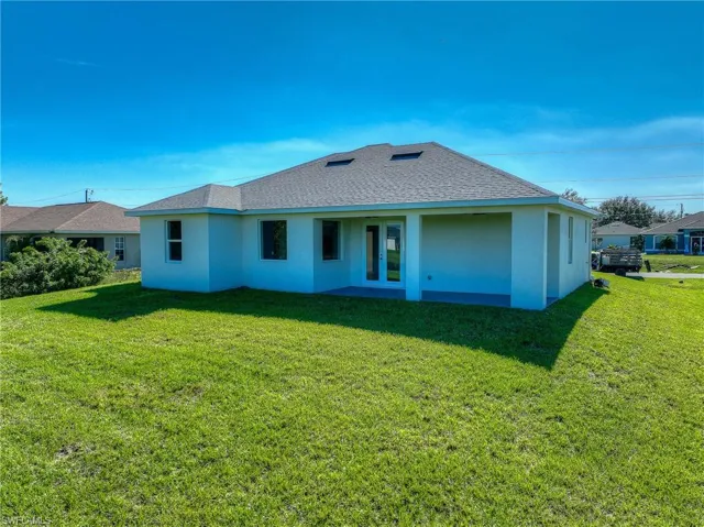 Back of property featuring a shingled roof, stucco siding, and a lawn