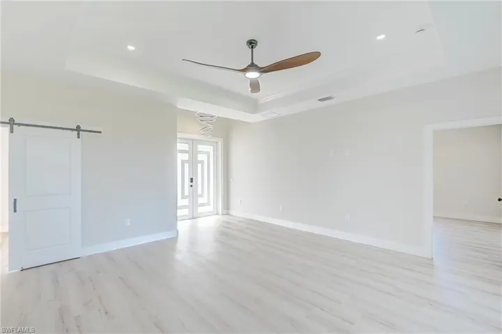 Empty room with a tray ceiling, french doors, light wood-type flooring, a ceiling fan, and recessed lighting