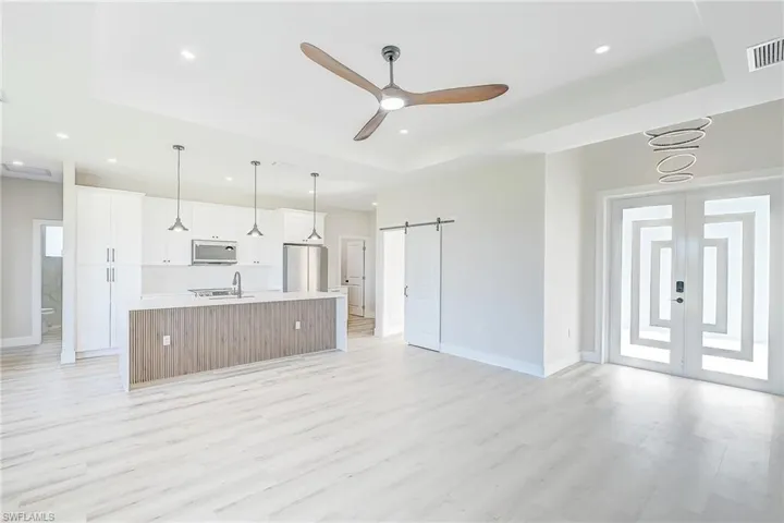Unfurnished living room with a barn door, a tray ceiling, light wood-style flooring, a ceiling fan, and recessed lighting