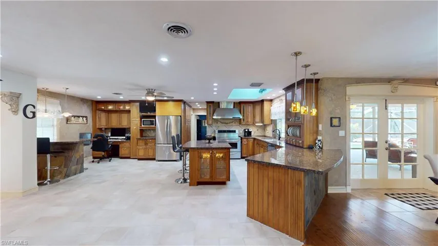 Kitchen featuring a kitchen bar, dark stone countertops, brown cabinetry, decorative light fixtures, and appliances with stainless steel finishes