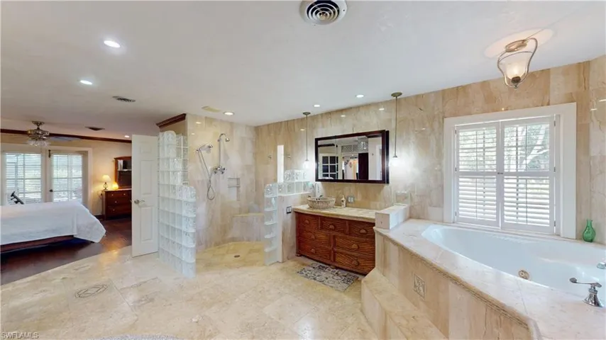 Ensuite bathroom with healthy amount of natural light, a whirlpool tub, walk in shower, vanity, and tile walls