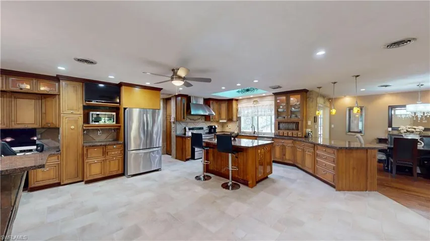 Kitchen with a kitchen bar, glass insert cabinets, brown cabinetry, a peninsula, and recessed lighting