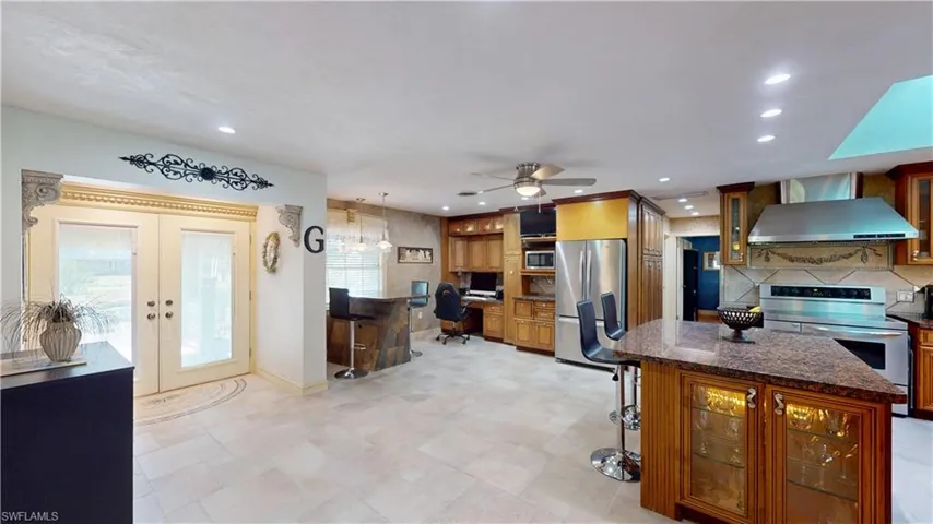 Kitchen featuring glass insert cabinets, a kitchen breakfast bar, stainless steel appliances, a kitchen island, and wall chimney range hood