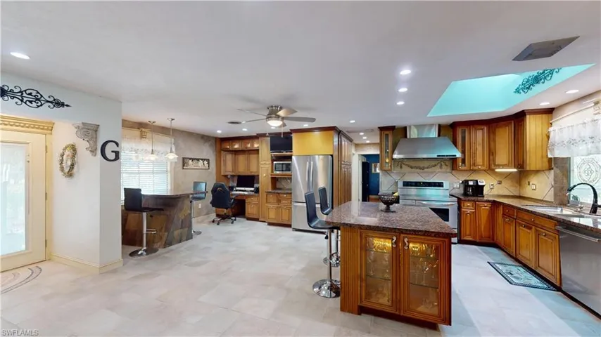 Kitchen with a breakfast bar, dark stone counters, stainless steel appliances, glass insert cabinets, and recessed lighting
