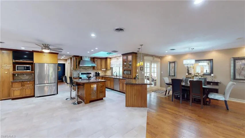 Kitchen with a breakfast bar area, brown cabinets, stainless steel appliances, tasteful backsplash, and wall chimney exhaust hood
