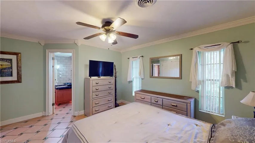 Bedroom featuring crown molding, ceiling fan, light tile patterned flooring, and ensuite bath