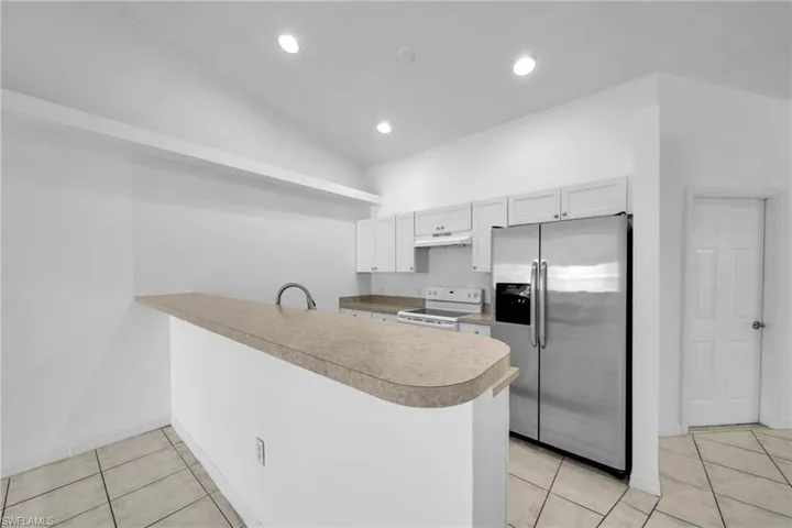 Kitchen featuring white shaker cabinetry, stainless steel appliances, a breakfast bar, and light-toned tile flooring