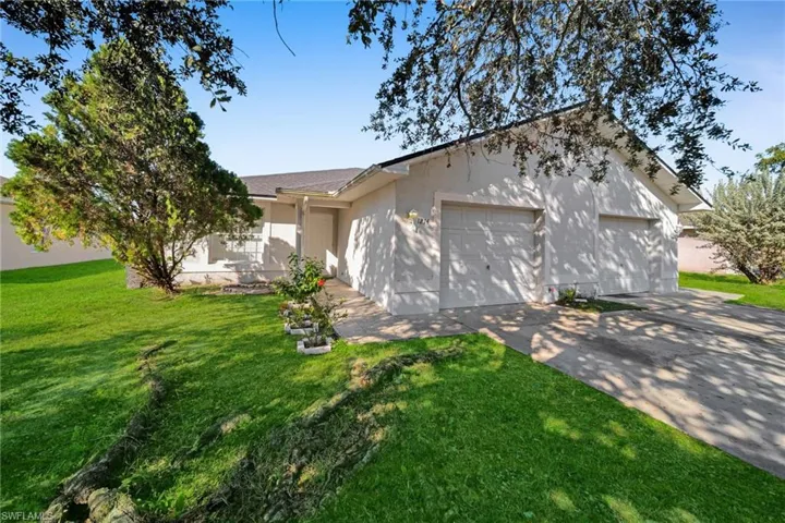 Exterior featuring a stucco finish, a two-car garage, a concrete driveway, and a front lawn with established landscaping