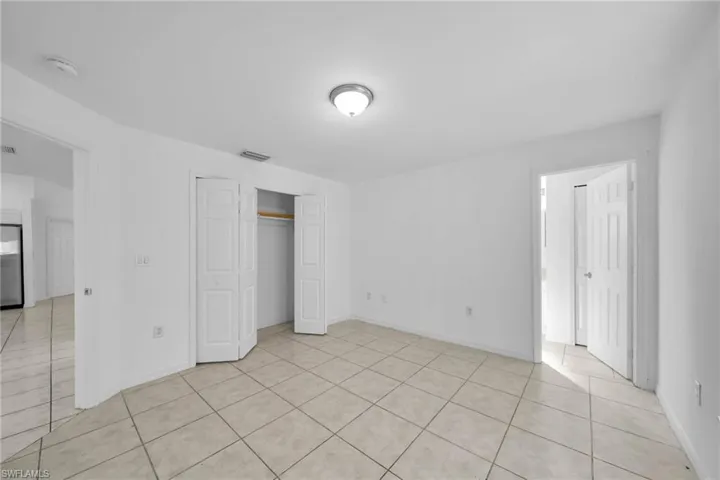 Spacious room featuring neutral tile flooring, white painted walls, a flush-mount ceiling light fixture, and a bi-fold closet with an interior hanging rod