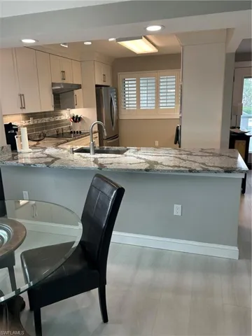 Kitchen with kitchen peninsula, white cabinetry, fridge, and light stone counters