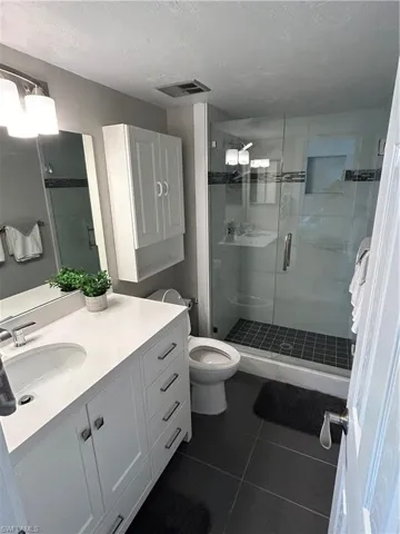 Bathroom with tile patterned floors, walk in shower, vanity, a textured ceiling, and toilet
