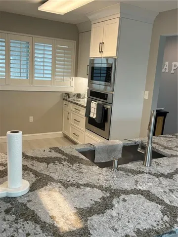 Kitchen with white cabinets, stone counters, oven, and light wood-type flooring